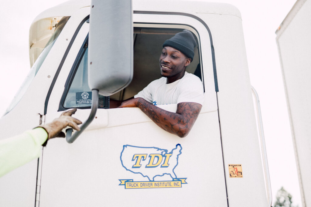TDI student sits in the cab of a parked white TDI semi truck. He looks down at his instructor, who's out of the frame.